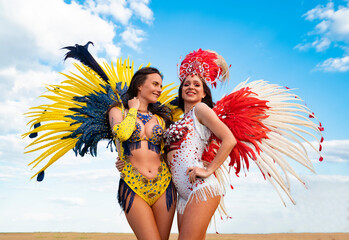 Two beautiful exotic Samba dancers hugging each other and smiling , sky background 