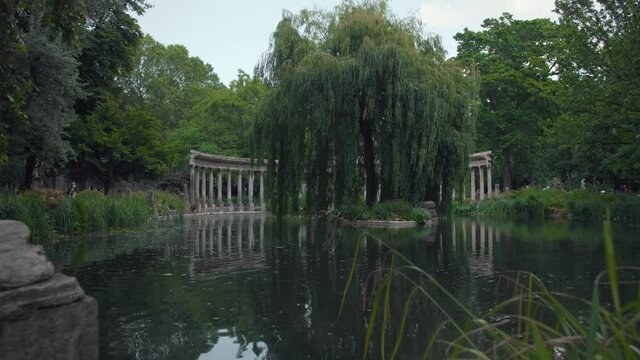 Panning across Parc Monceau with colonnade, beautiful trees and lake on cloudy day in Paris, France.