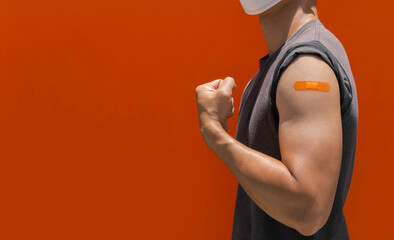 Vaccinations, bandage plaster on vaccinated people's arm concept. Orange color adhesive bandage on the strong man's arm who fist hand and showing muscle after vaccination treatment with copy space. - obrazy, fototapety, plakaty