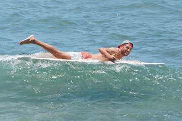 A happy Surfer shows a thumbs up gesture while swimming on a board in the ocean in tropical warm water.