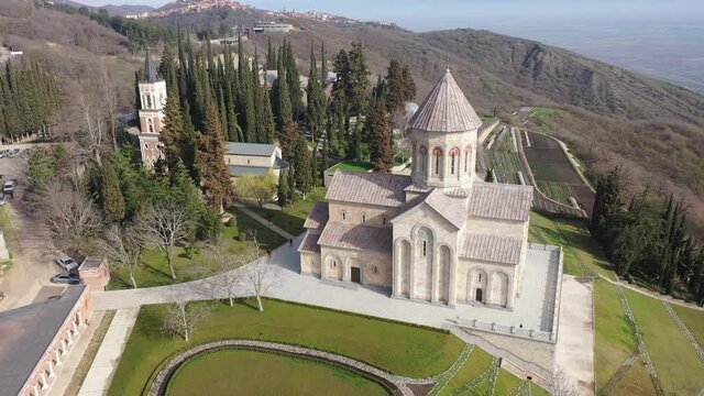 Scenic spring aerial view of Church of St. Nino in monastic complex of Bodbe nunnery on hillside overlooking Alazani Valley and Greater Caucasus mountains in background, Sighnaghi, Kakheti, Georgia. 