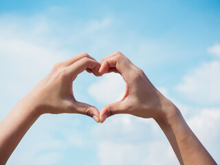 Heart shape hand on blue sky and fluffy cloud background, concept of love, relationship and...