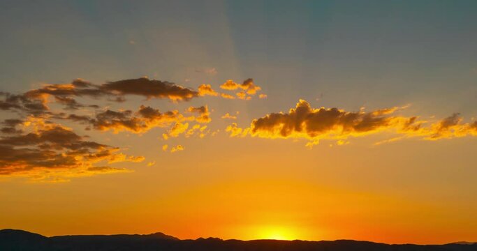 The sun sets behind the mountains in golden splendor as another day comes to an end - static time lapse with