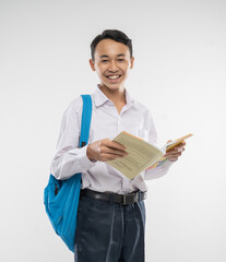 a boy smiles at the camera wearing a school uniform and backpack while reading a book in an...