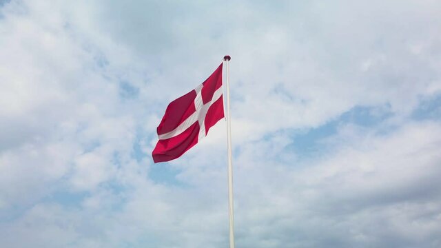 Danish flag waving in the wind, on a blue sky with white clouds, on a beautiful summer day. Just the top of the flag pole and the whole flag is in frame. 4K