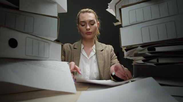 Tired woman with pile of folders working in office, female employee works with documents in evening having headache, exhausted worker with red eyes reading documentation. Fatigue, lots of work. 