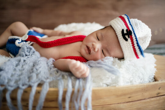 newborn baby boy wearing a white and blue sailor hat. He is sleeping on his back in a tiny boat.