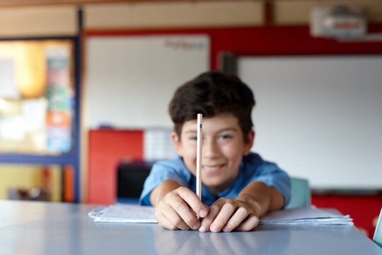 Young boy student in school classroom holding HB pencil