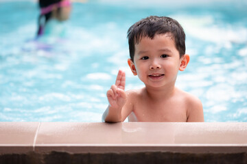 Fototapeta na wymiar Portrait of asian little boy looking at camera and smiling while playing water in the swimming pool. Summer activity and childhood lifestyle concept.