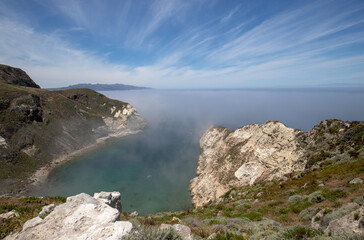 Fototapeta na wymiar Inversion layer clouds misting over Potato Harbor on Santa Cruz Island with mist coming in under blue cirrus sky in the Channel Islands National Park offshore from Santa Barbara California USA