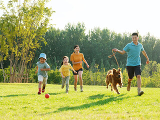 Happy family of four and pet dog playing in the park