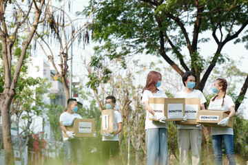 Group of young volunteers in medical masks gathering in park to collect donations for charitable foundation