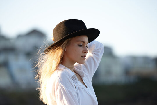 Carefree young blonde-haired woman at beach wearing black hat