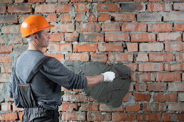 a man builder in a protective helmet plastering the wall with cement mortar. The foreman is engaged...