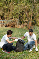 Voluteers collecting fallen leaves in big trash bags in city park