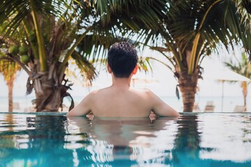 Asian happy man swimming and relax in swimming pool at resort hotel by the sea background on weekend vacation.Concept of happy solo travel.