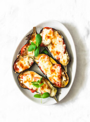 Mediterranean style baked eggplant with mozzarella and tomatoes on a light background, top view