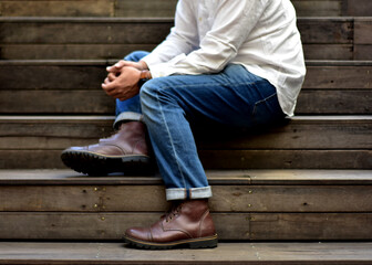 a man using boots and jeans sitting on the wood staircase