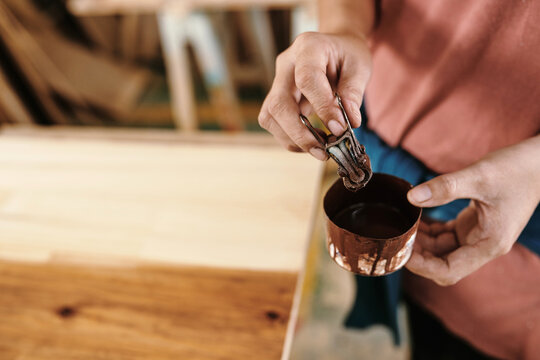 Close-up imege of female carpenter soaking binder clip with piece of cloth in jar with oil to cover wooden surface
