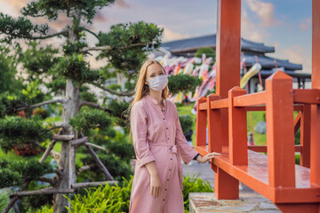 Woman traveler in medical mask looking at the Japanese traditional building. Tourists travel in Japan after the coronavirus epidemic