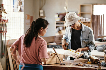 Young carpenters working on project, they are measurig wooden planks at workbench