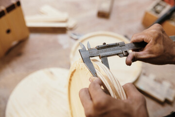 Hands of carpenter using mechanical vernier caliper when measuring thickness of wooden products