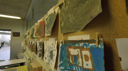 Children's paintings and drawings hanging on classroom wall interior on display closeup push forward