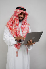 an arabian in a turban smiling while using a laptop computer on a plain background