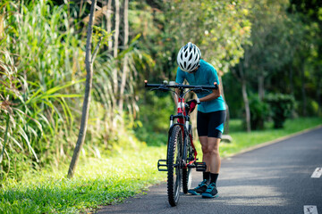 Fototapeta na wymiar Woman cyclist adjust the seat height cycling on summer park trail