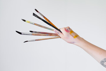 The hand of a girl artist holds a brush for painting on a white background.