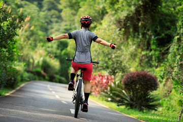 Naklejka premium Woman no handed cycling on tropical park trail in summer