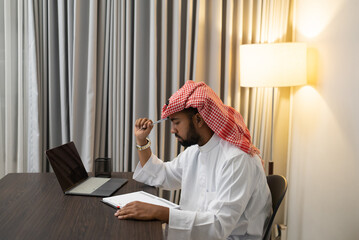 a young Arab entrepreneur who is working writing books with a pen and using a laptop at his desk