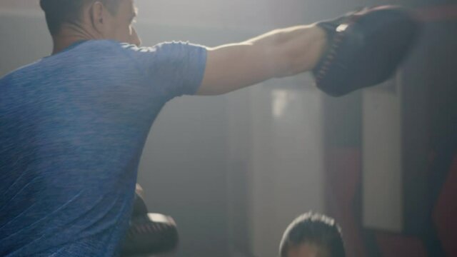 Asian beautiful young woman exercise with trainer at boxing gloves and self defense lesson punching, Female kickboxing training with male Instructor fight at fitness GYM, workout healthy sport concept
