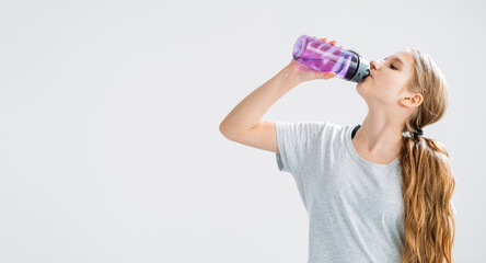 Fitness hydration. Sport banner. Fresh start. Kids healthy lifestyle. Thirsty athletic girl drinking mineral water from bottle isolated on light copy space background.