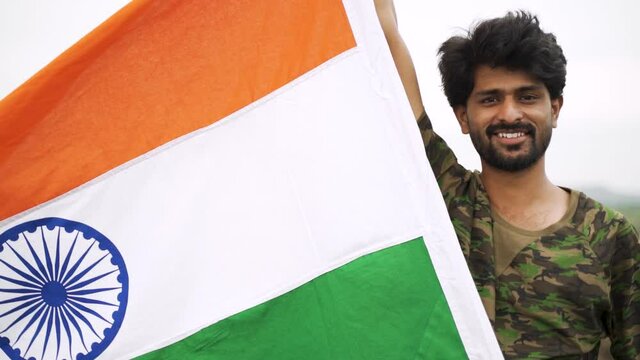 Medium Close Young smiling man holding waving Indian flag on top of mountain - Concept of patriotism, celebration Independence or republic day celebration