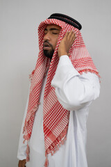 An Arab muezzin in a turban performs the call to prayer with one hand beside his ear on a plain...