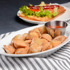 Fried dumplings stuffed with meat and served with tomato sauce on a white plate.