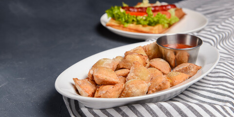 Fried dumplings stuffed with meat and served with tomato sauce on a white plate.