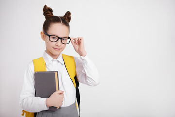 portrait of cute girl in school uniform and eyeglasses with backpack and book posing over white...