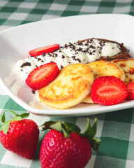 Cottage cheese pancakes, syrniki, ricotta fritters on ceramic plate with fresh strawberry.