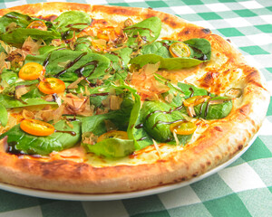 Delicious pizza with spinach and tuna shavings served on wooden table with green plaid tablecloth.