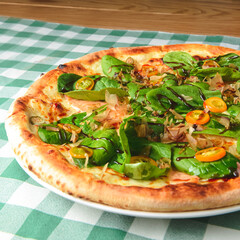 Delicious pizza with spinach and tuna shavings served on wooden table with green plaid tablecloth.