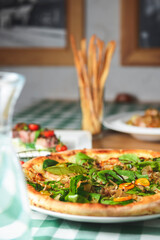 Delicious pizza with spinach and tuna shavings served on wooden table with green plaid tablecloth.