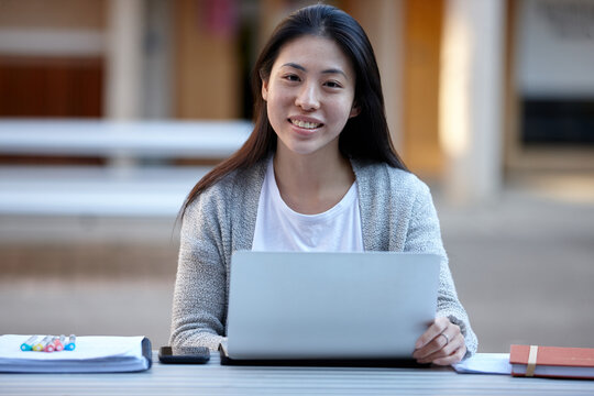 Young Asian female university student studying on laptop outdoors