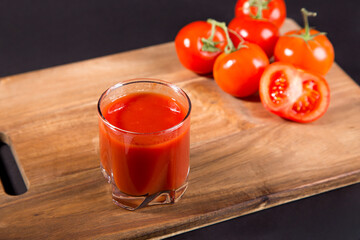 Tomato juice in a glass and fresh tomatoes on the table