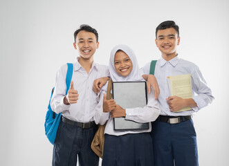 Three teenagers in junior high school uniforms holding a laptop computer with thumbs up when carrying school bag and a book on an isolated background