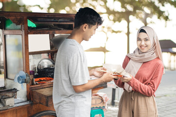 Fototapeta na wymiar muslim woman ordering chicken satay from small food cart seller. sate ayam street food