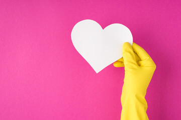 Top view photo of hand in yellow glove holding white paper heart on isolated pink background with copyspace