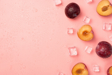 Top view photo of halves and whole plums ice cubes on the right and water drops on isolated pastel pink background with copyspace on the left