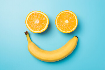Top view photo of smiling face made from two orange halves and yellow banana on isolated pastel blue background